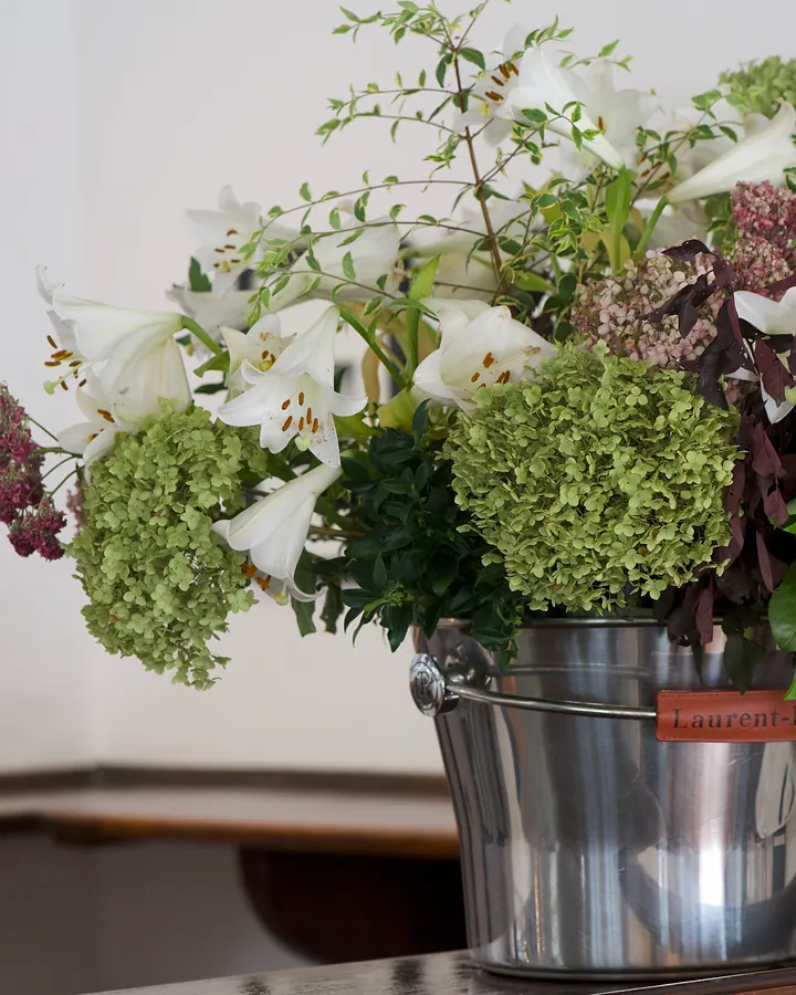 A bucket of fresh lilies, hydrangeas and greenery on a wooden counter at Bellinis