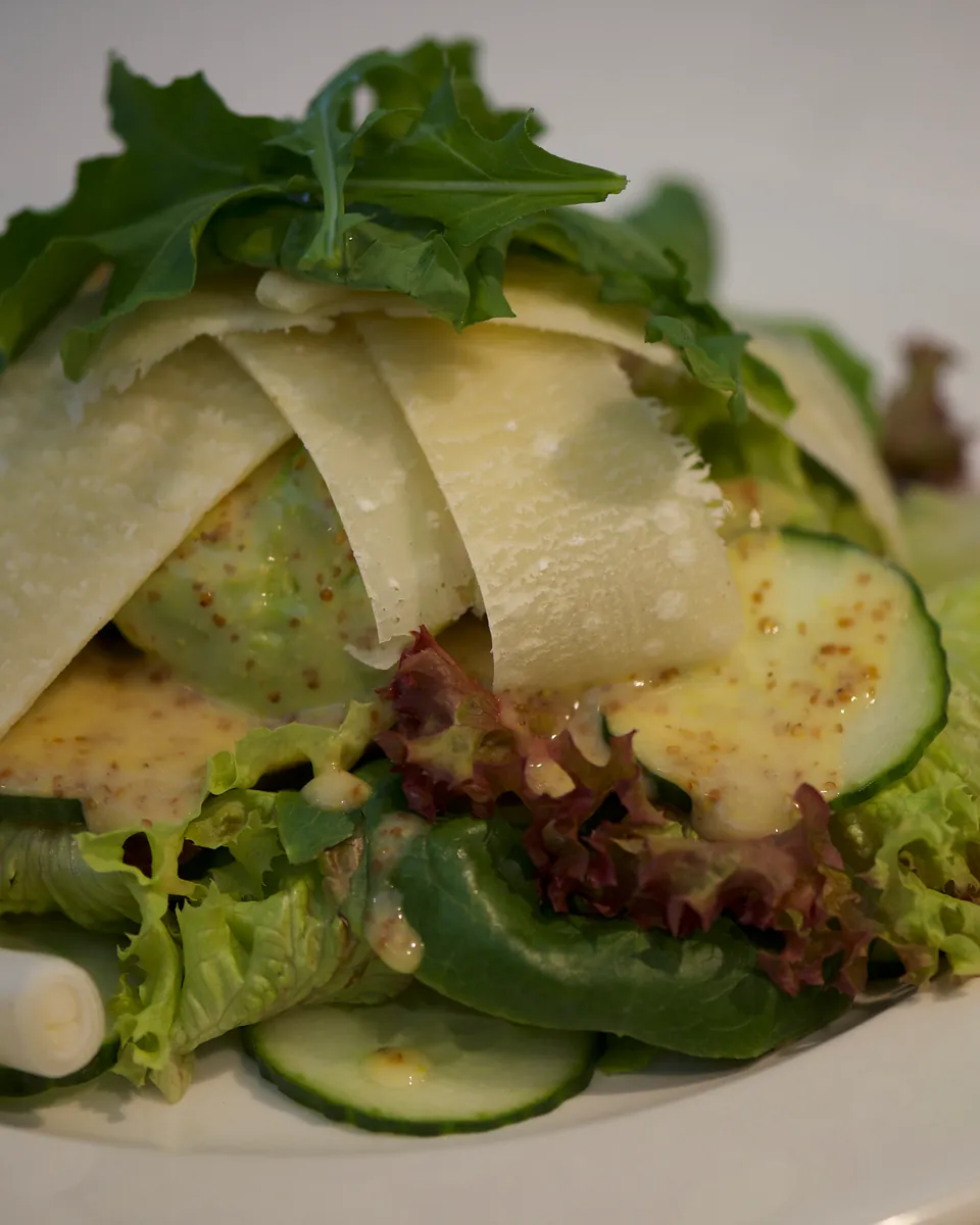Green salad topped with shaved Parmesan, avocado, cucumber and rocket